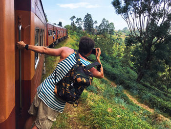 Rear view of man photographing landscape while standing at train entrance