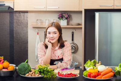 Portrait of young woman with various vegetables in kitchen