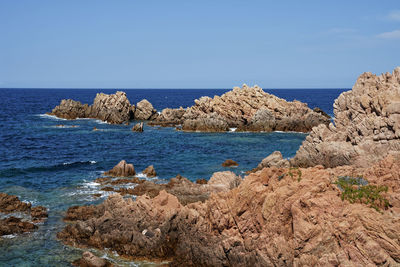 Scenic view of rocks in sea against clear blue sky
