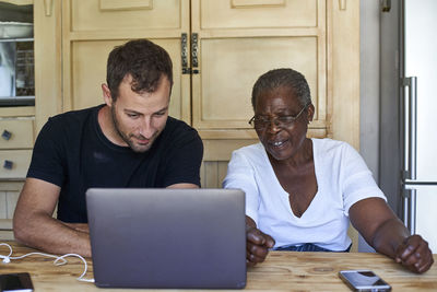 Senior woman and man sitting at kitchen table sharing laptop