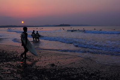 Surfer walking at beach against orange sky