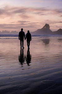 Silhouette men standing on beach against sky during sunset