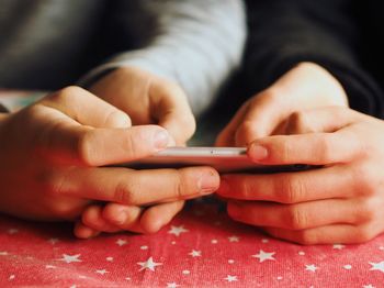 Cropped hands of friends using phone at table