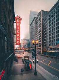 Illuminated street amidst buildings against sky at dusk