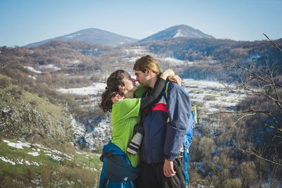Couple kissing while standing on mountain against sky