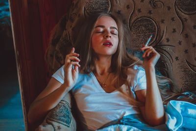 Young woman with eyes closed smoking cigarette at home