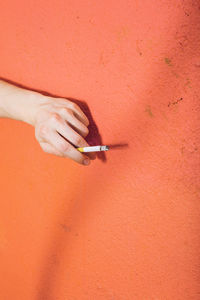 Close-up of hand holding cigarette against wall