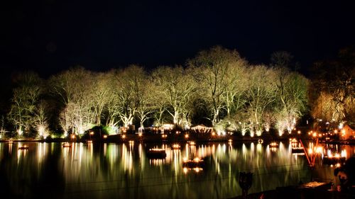 Illuminated trees by river against sky at night