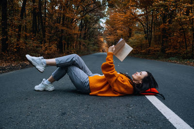 Confidence woman with book sitting on the road with autumn tree around. new life, path choice