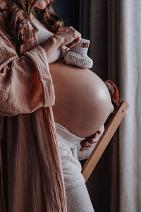 Pregnant woman with mug of hot herbal tea staying in front of window. expecting new baby