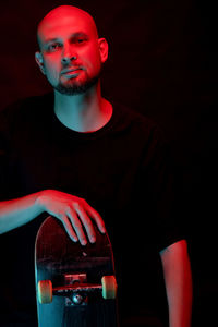 Portrait of man with skateboard against black background