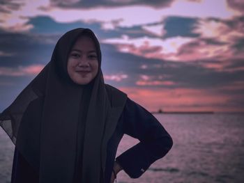 Portrait of smiling woman standing against sea during sunset