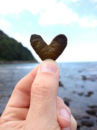 Close-up of hand holding heart shape against sea