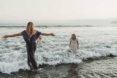 Mom and two young girls splashing in ocean at sunset