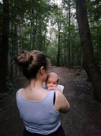 Rear view of mother carrying baby boy in forest