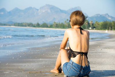 Rear view of young woman sitting at beach against clear sky