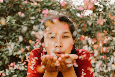 Portrait of young woman blowing flower petals against plants