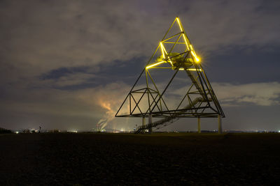 Illuminated ferris wheel on field against sky at sunset