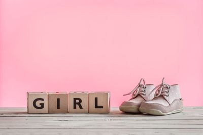 Close-up of shoes with girl text on table against pink background