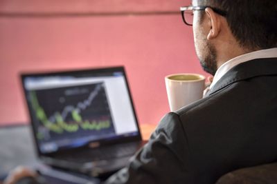 Rear view of businessman having coffee while working on laptop in office