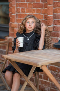 Portrait of a young woman sitting on chair against brick wall