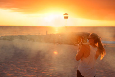 Woman standing on shore against sky during sunset