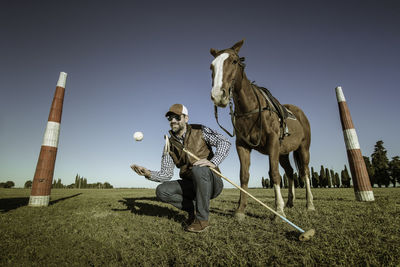 Man holding polo mallet while playing with ball by horse on field