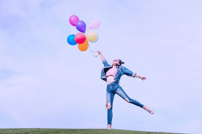 Low angle view of person holding balloons against sky