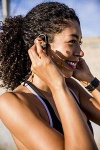 Close-up of female athlete adjusting headset while standing against sky