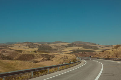 Empty road by mountains against clear blue sky