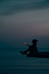 Rear view of man with arms raised in sea against sky during sunset