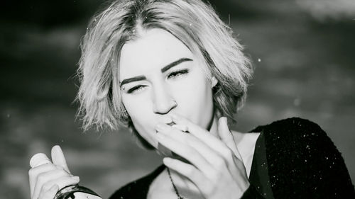 Close-up of young woman smoking cigarette while holding alcohol bottle at night