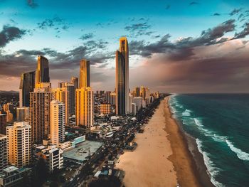 Modern buildings at beach against cloudy sky during sunset