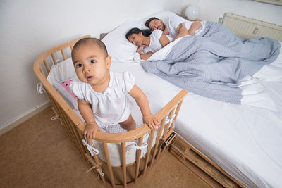 High angle view baby in crib while parents sleeping on bed at home