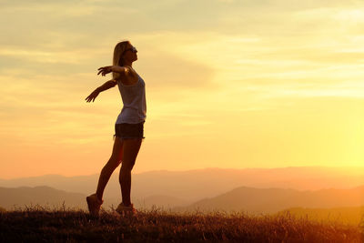 Rear view of woman standing against sky during sunset