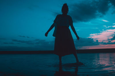 Rear view of woman standing by sea against sky