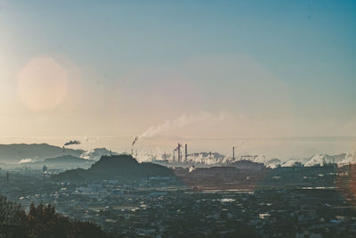 Cityscape and industry against sky during sunset