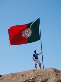 Low angle view of man with portuguese flag against clear blue sky