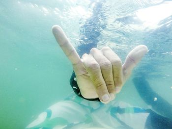 Cropped image of person showing horn sign while swimming in sea