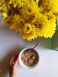 Cropped image of hand touching muesli on table by yellow flowers