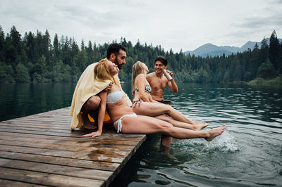 Rear view of couple sitting on lake against trees