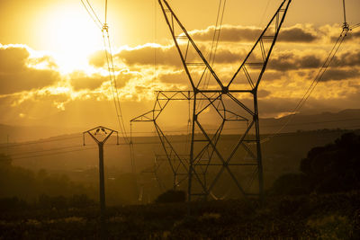 Low angle view of electricity pylon against sky during sunset