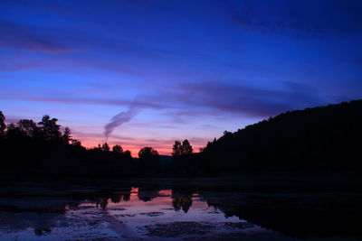 Silhouette trees by lake against sky at sunset