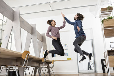 Two happy colleagues in office jumping and high fiving