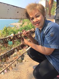 Woman crouching by railing by holding love lock outdoors