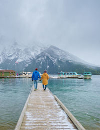 Rear view of woman walking on pier over sea against snowcapped mountain