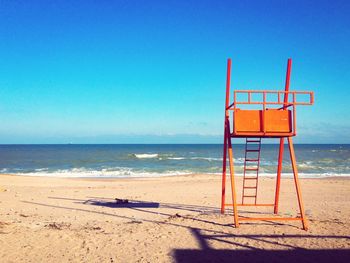 Lifeguard hut at shore of beach against blue sky