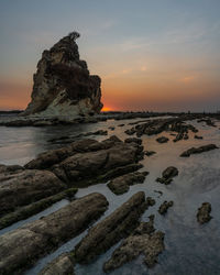 Rock formation on beach against sky during sunset