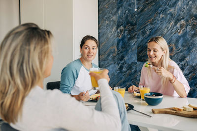 A group of female friends sitting at the table having breakfast and chatting.