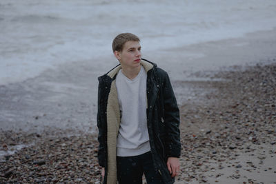 Portrait of a teenager with a serious face, immersed in himself, on a sandy seashore, cold stormy 